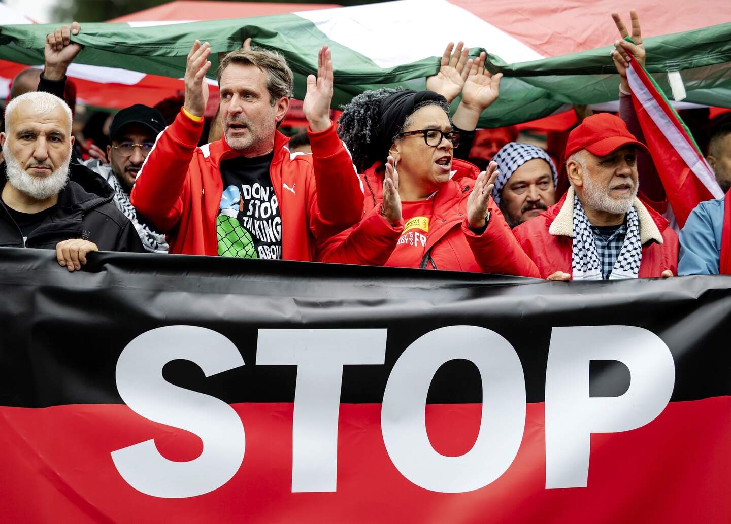 Michiel Servaes, directeur van Oxfam Novib, klapt in zijn handen tijdens een Rode Lijn-protest. Rechts, met rode pet en grijze baard: Adnan Adass.