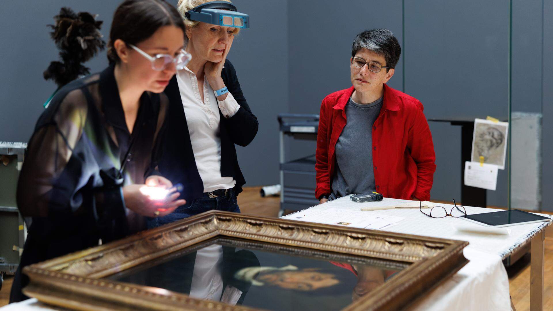 Kunstenares Fiona Tan (in rode jasje) bekijkt met de twee conservatoren het portret van een kleptomaan van Géricault.  