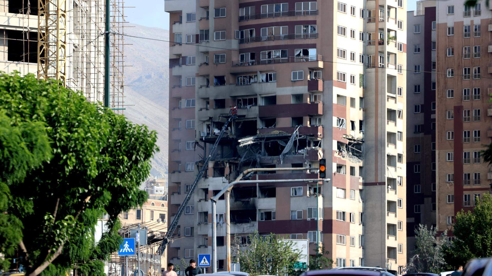 People walk past traffic in front of a building targeted by an Israeli strike in the Iranian capital Tehran on June 13, 2025. Israel carried out strikes against Iran early on June 13, targeting its nuclear and military sites as well as residential buildings in Tehran, after US President Donald Trump warned of a possible "massive conflict" in the region.
ATTA KENARE / AFP